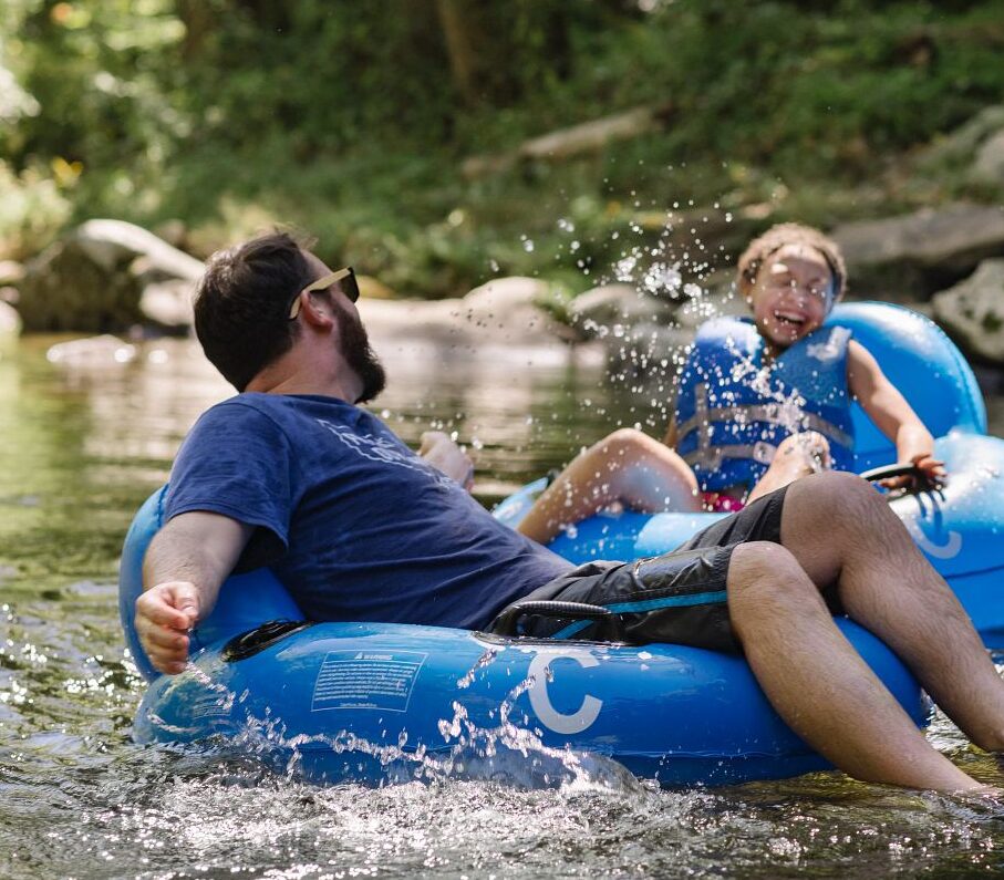 father splashing daughter while tubing down a river in the mountains