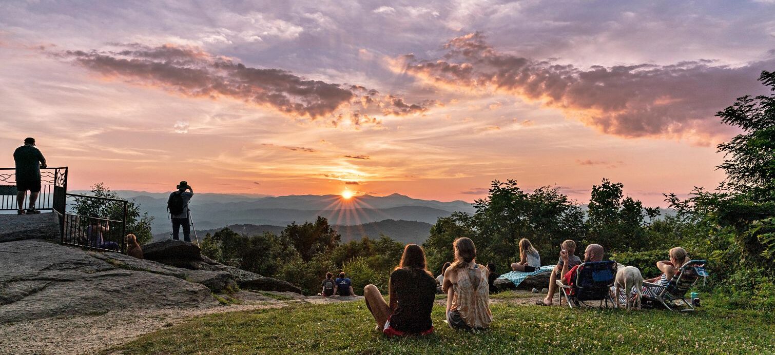 groups of people sitting in the grass to watch the sunset at jump off rock