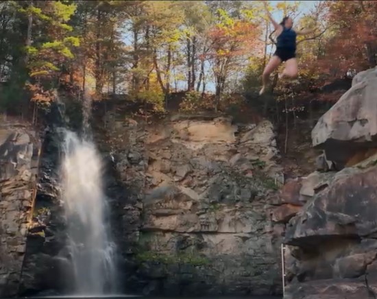 girl cliff jumping near waterfall