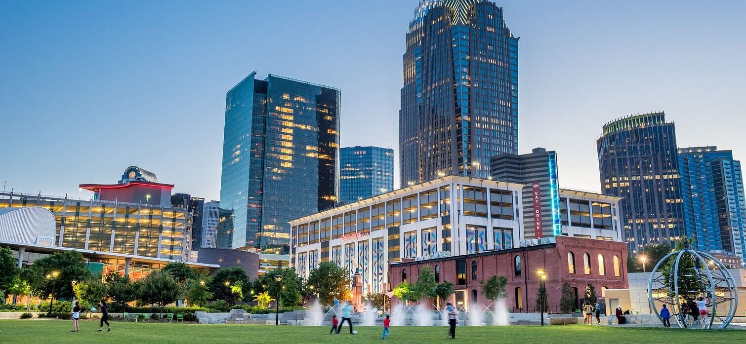 Uptown skyline, photographed from First Ward Park at dusk, with kids and families playing in the park in the foreground