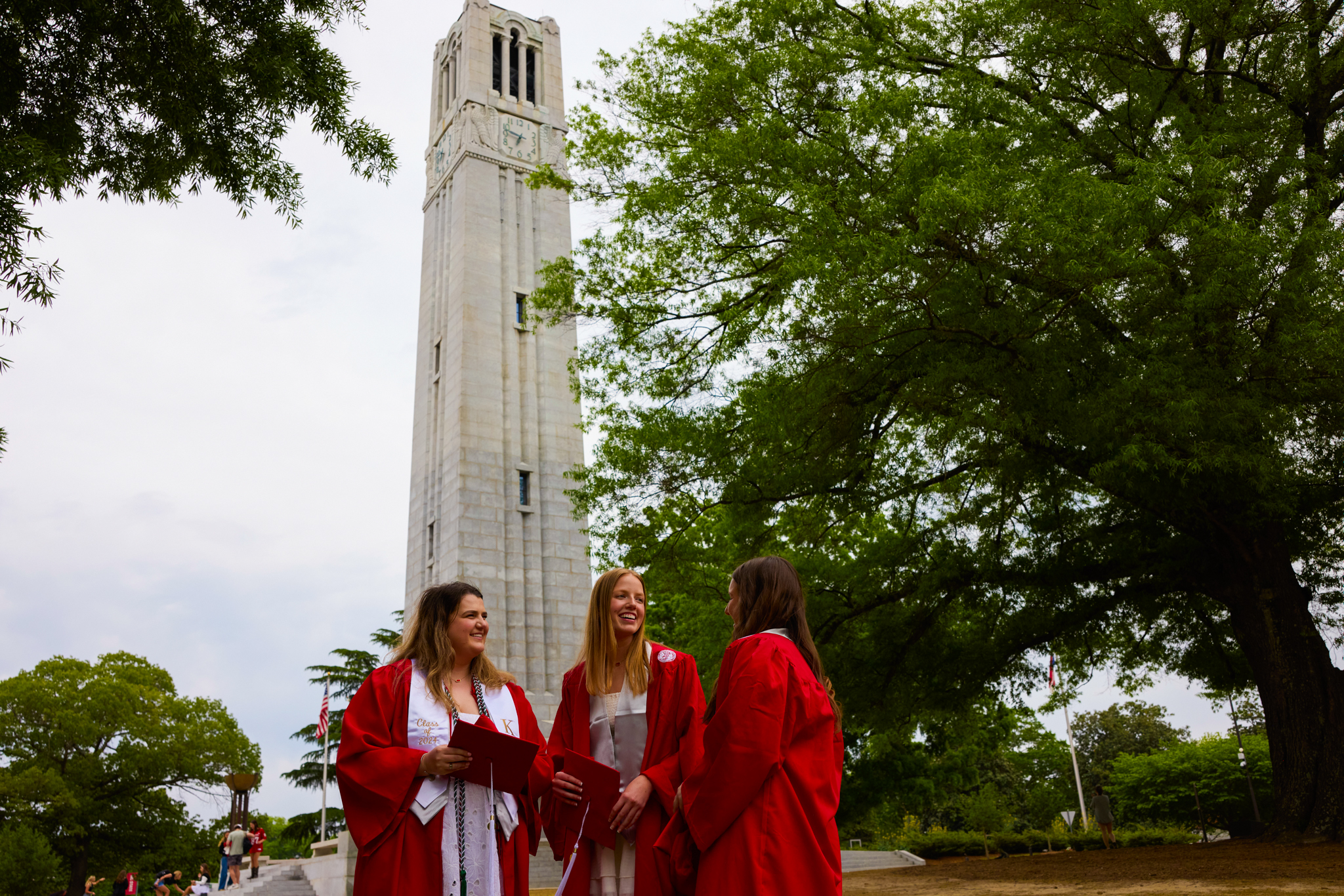 a group of NC State graduates standing in front of the memorial bell tower